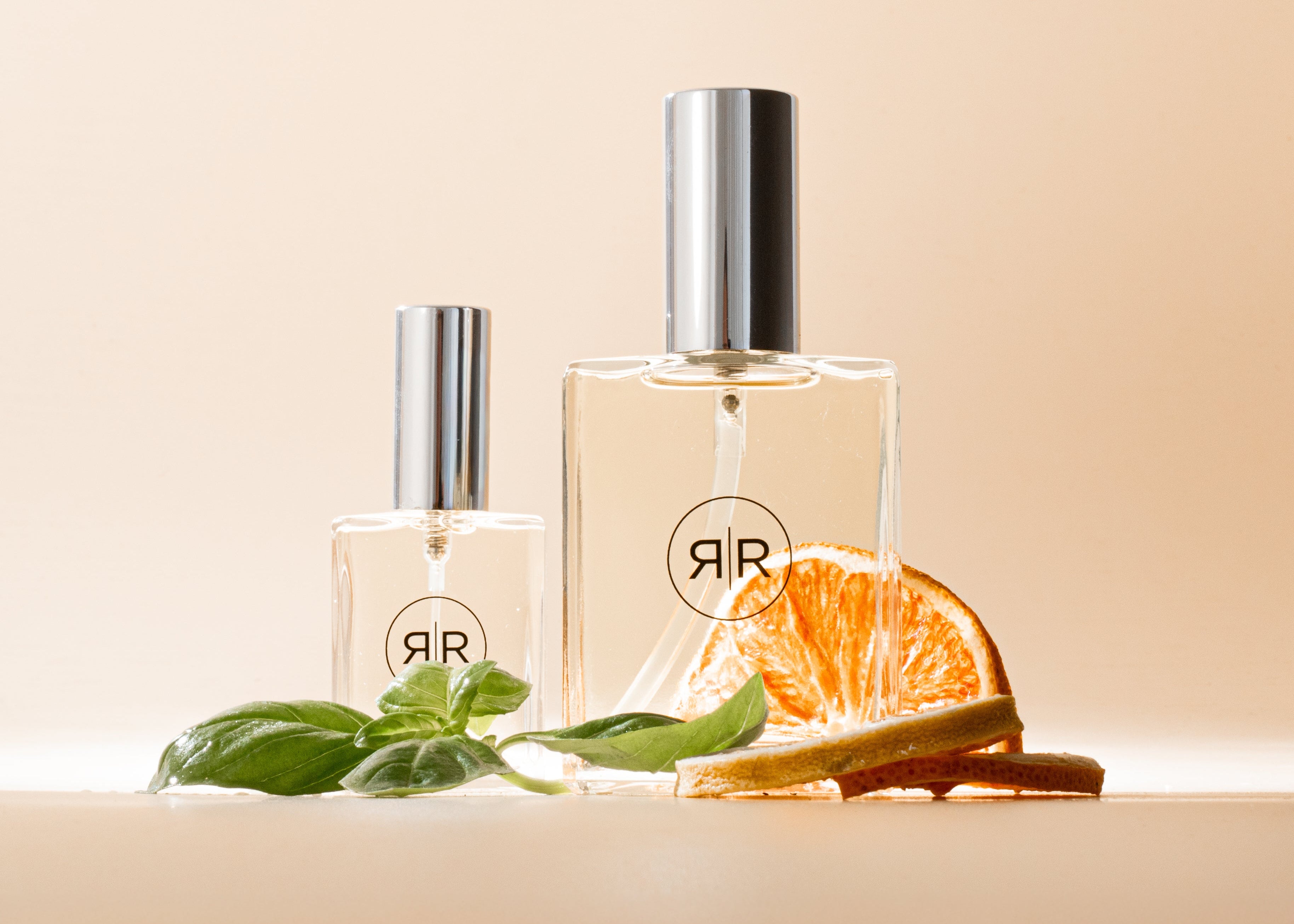 Two perfume bottles with a slice of orange and basil leaves on a beige background